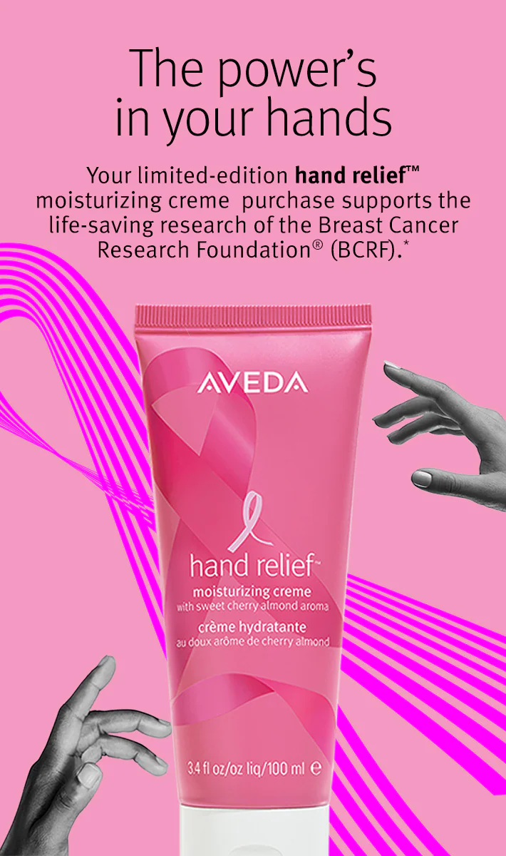 A tube of Aveda hand relief moisturizing creme with breast cancer awareness branding is shown on a pink background with text about supporting breast cancer research. - Trios Aveda Salon | Fort Collins, CO
