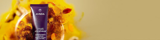 Aveda Invati Advanced tube displayed in front of vibrant yellow and orange botanicals on a yellow background—perfect for holiday hair prep and stunning seasonal hairstyles. - Trios Aveda Salon | Fort Collins, CO