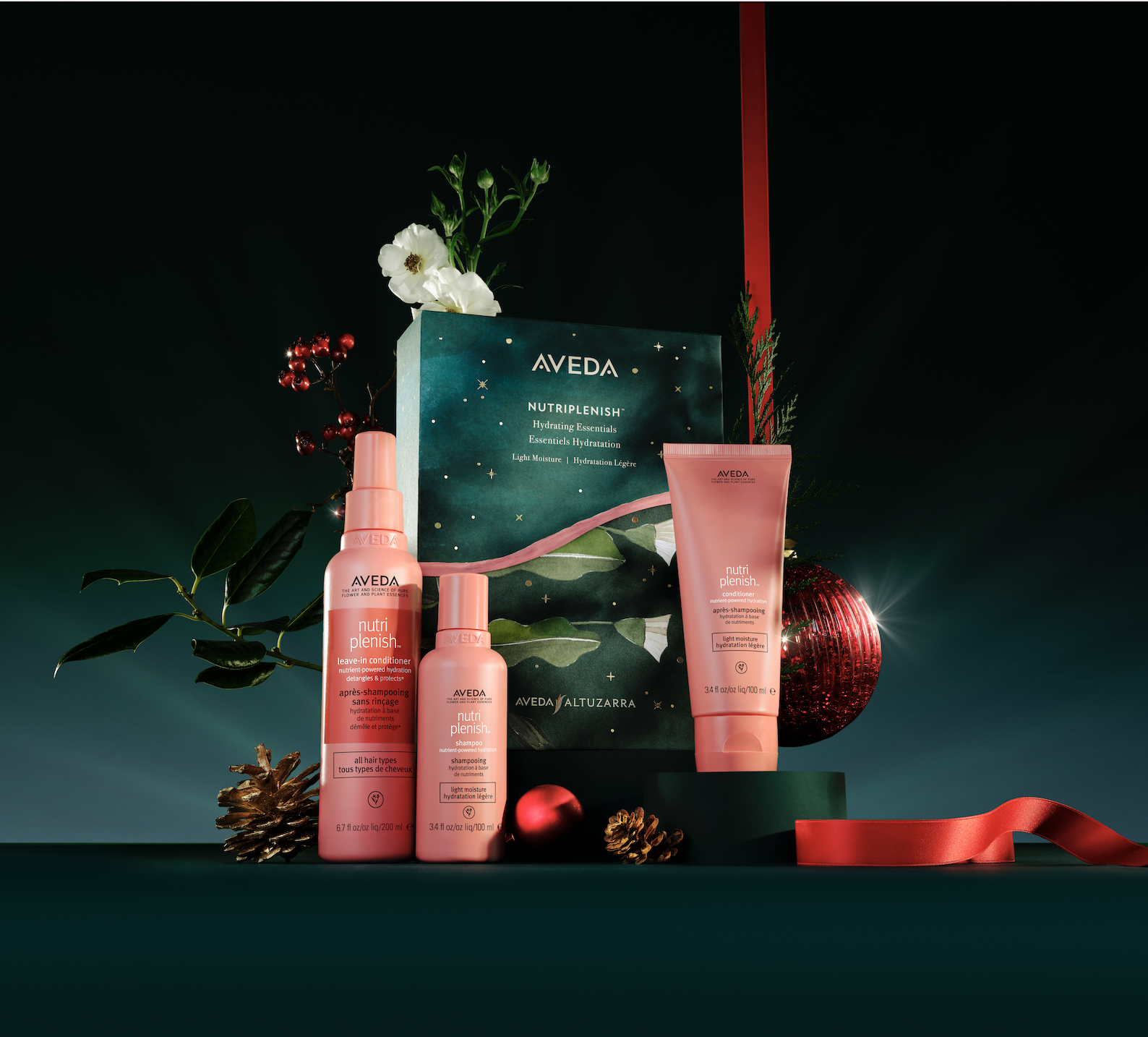 Aveda NutriPlenish hair care set with bottles and a box displayed on a dark background, accented with flowers, pine cones, and red holiday ornaments. - Trios Aveda Salon | Fort Collins, CO