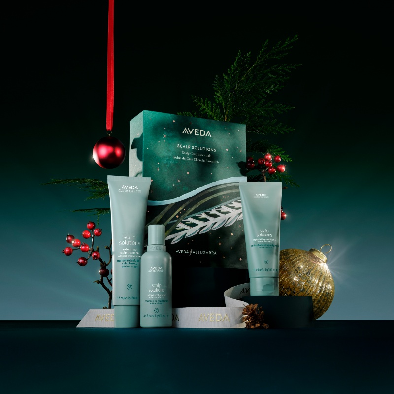 Aveda Scalp Solutions products arranged with festive decor, including a gold ornament and red berries, set against a dark background. - Trios Aveda Salon | Fort Collins, CO