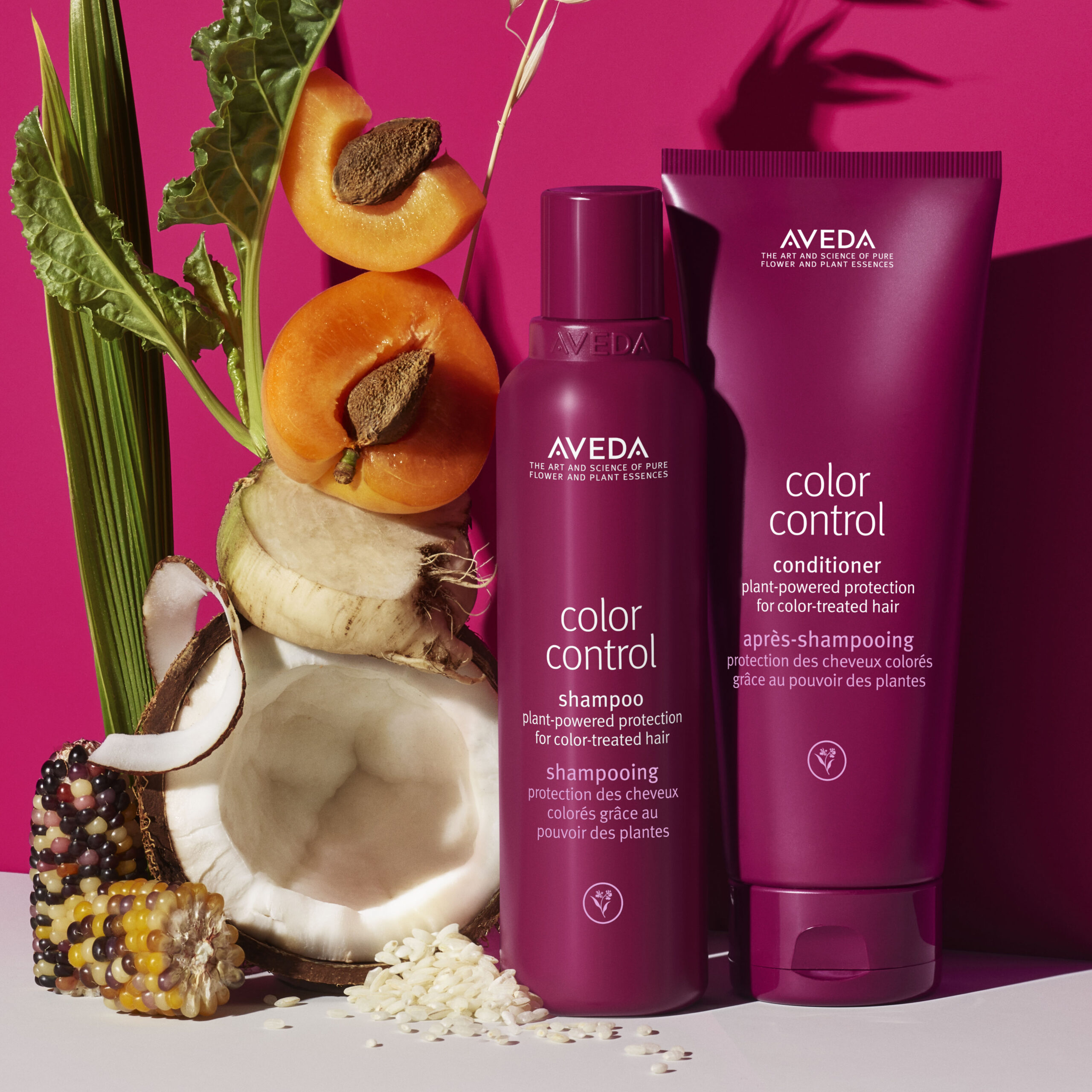 Aveda Color Control shampoo and conditioner bottles on a pink background, surrounded by plant elements like corn, apricot, and beet. - Trios Aveda Salon | Fort Collins, CO